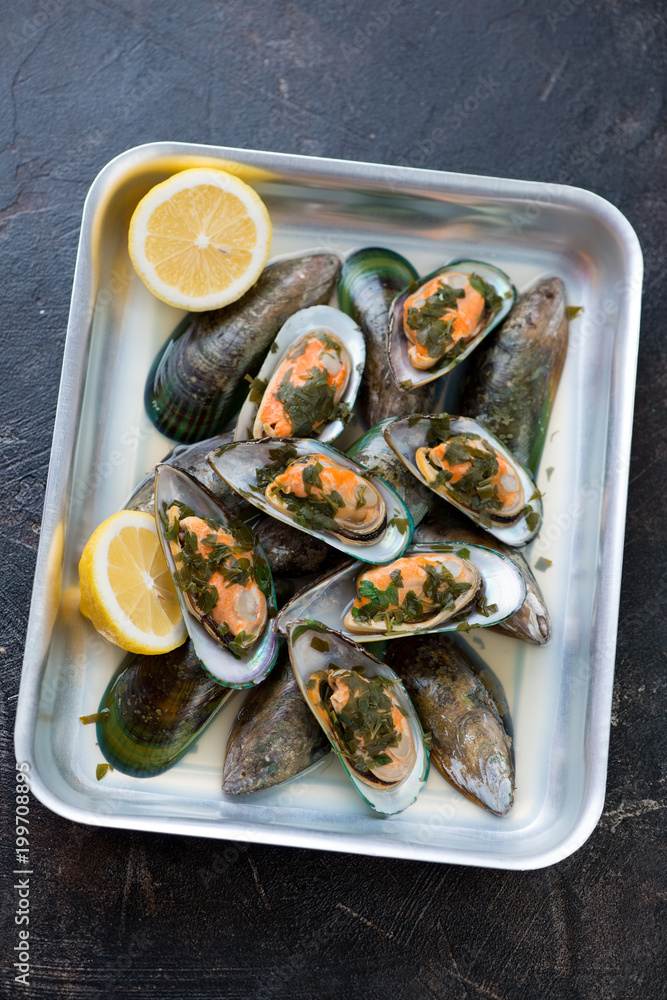 Baking tray with kiwi mussels stewed in white wine, brown stone surface, vertical shot Baking tray with kiwi mussels stewed in white wine, brown stone surface, vertical shot