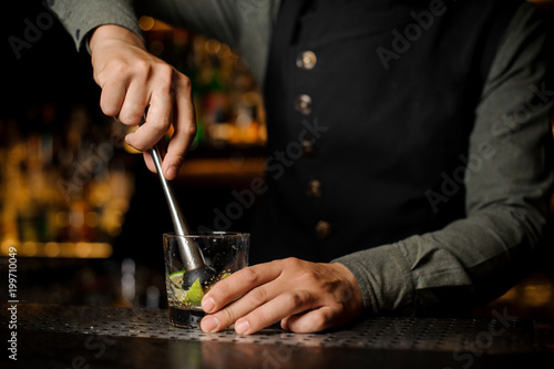 Barman mixing a cane sugar with lime in the glass