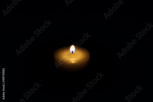 Burning wick of a wax round candle in complete darkness on a black background.
