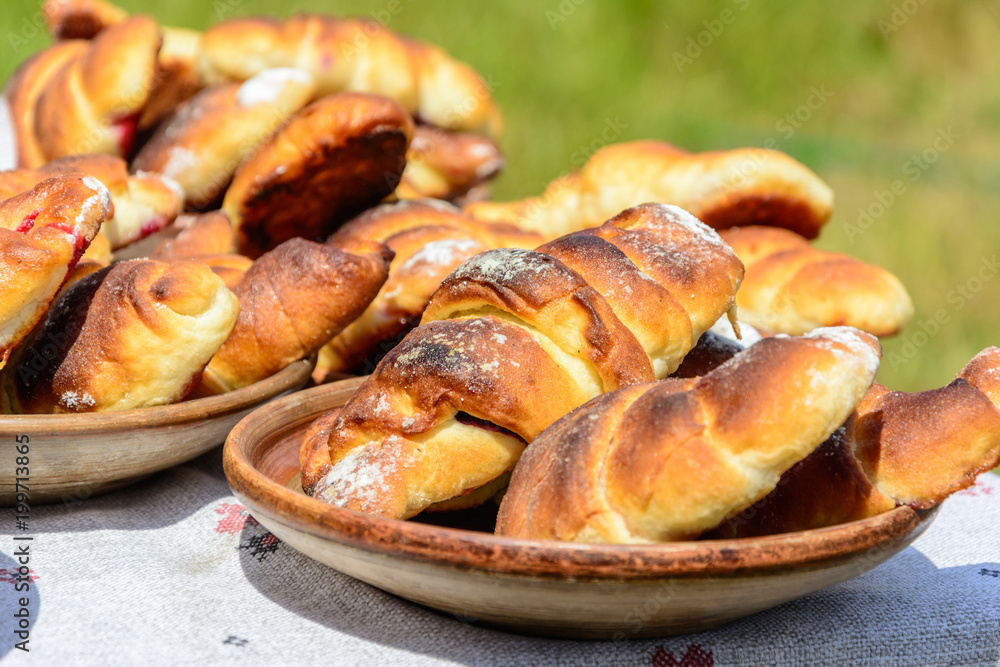 Fresh buns and cupcakes are on the table that is situated outdoors. This is dishes of the Ukranian cuisine. Fresh buns and cupcakes are on the table that is situated outdoors. This is dishes of the Ukranian cuisine.