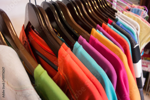 Line of multi colored clothes on wooden hangers in store. Sale