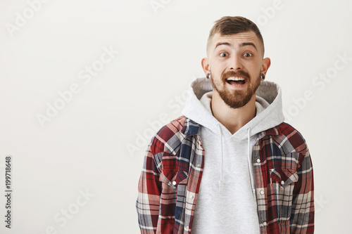 Brother happy to receive new skateboard. Pleased amazed good-looking guy with trendy outfit and hairstyle wearing flesh tunnels in ears, dropping jaw and lifting eyebrows from surprise and happiness