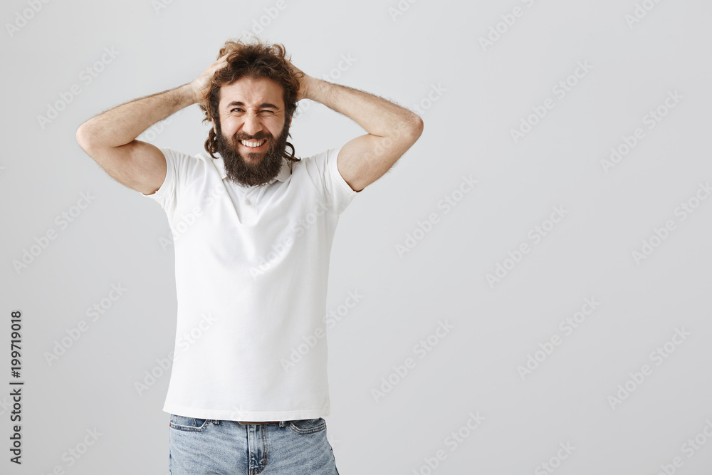 Carefree and happy handsome eastern man with beard and curly hair holding hands on head while winking and smiling broadly, being glad to have day off and spending it at home with family Carefree and happy handsome eastern man with beard and curly hair holding hands on head while winking and smiling broadly, being glad to have day off and spending it at home with family
