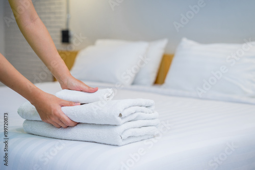 Close-up of hands putting stack of fresh white bath towels on the bed sheet. Room service maid cleaning hotel room.
