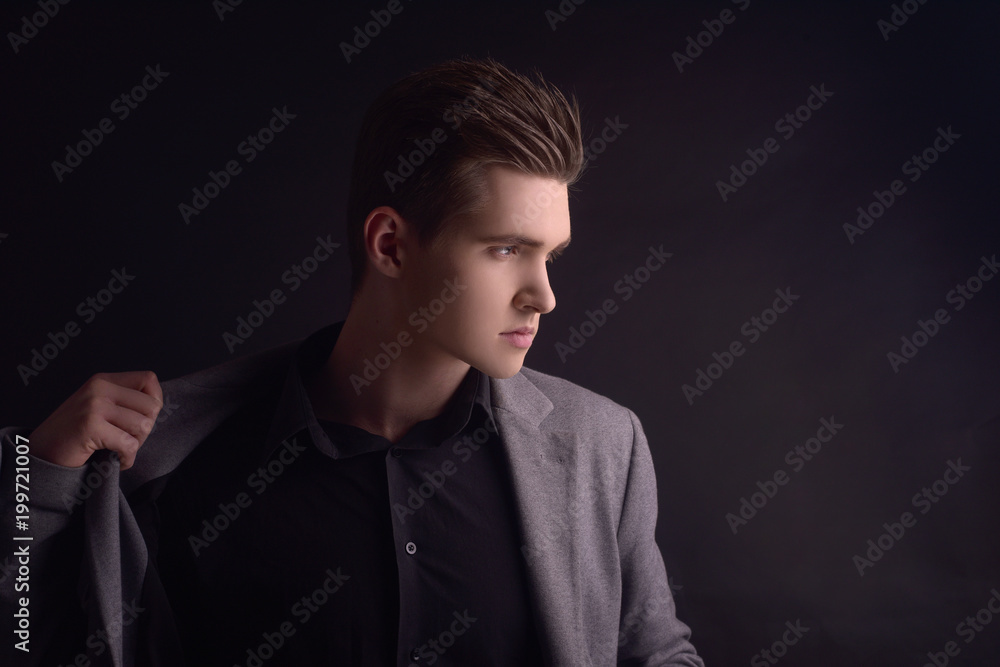 Young handsome man in coat. Portrait of fashionable well dressed man posing in grey stylish coat. Confident and focused boy on black background. Elegant man with perfect hairstyle. Male hair styling.