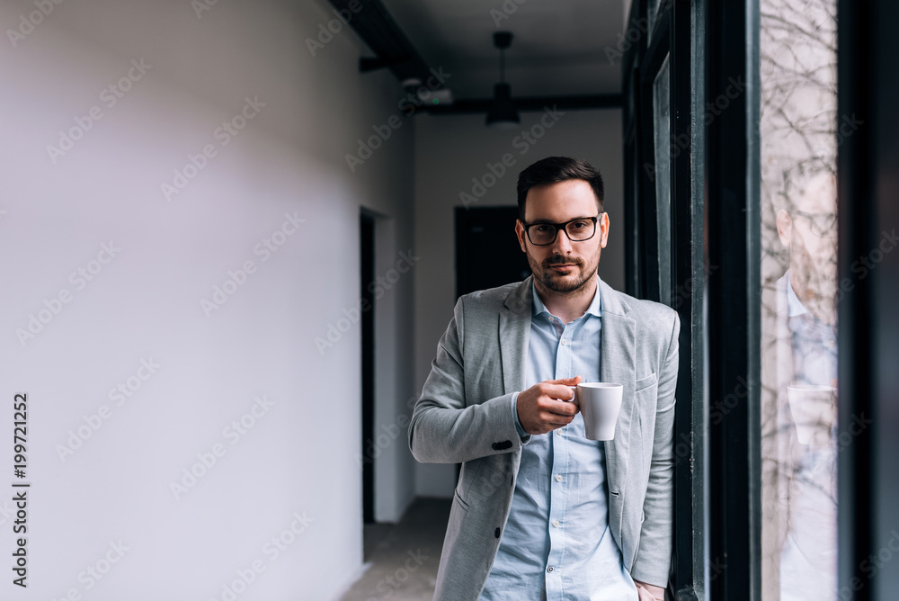 Portrait of a handsome man holding a mug in the hallway near the window. Looking at camera. Portrait of a handsome man holding a mug in the hallway near the window. Looking at camera.