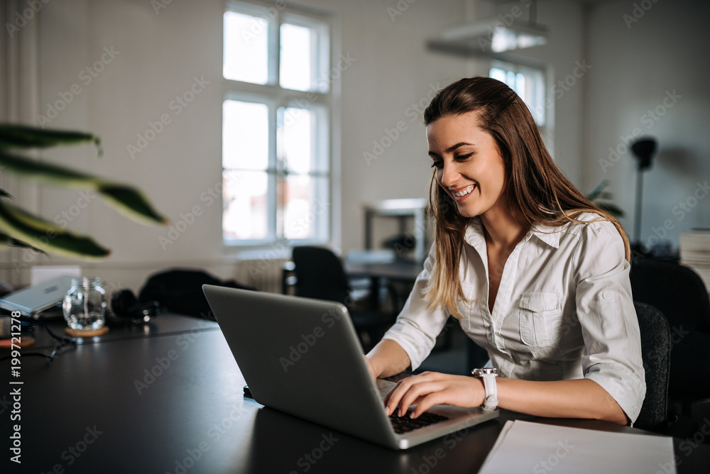Smiling brunette girl working on a laptop at modern office Smiling brunette girl working on a laptop at modern office