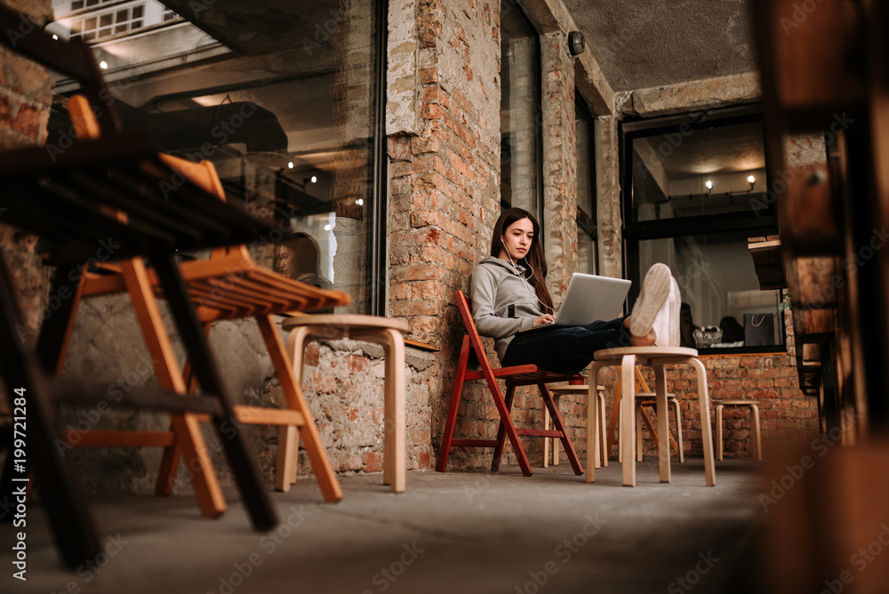 Casual girl relaxing using laptop at terrace with old brick walls.