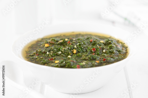 Raw homemade Argentinian green Chimichurri salsa or sauce made of parsley, garlic, oregano, hot pepper, olive oil, vinegar, photographed with natural light (Selective Focus in middle of the image)