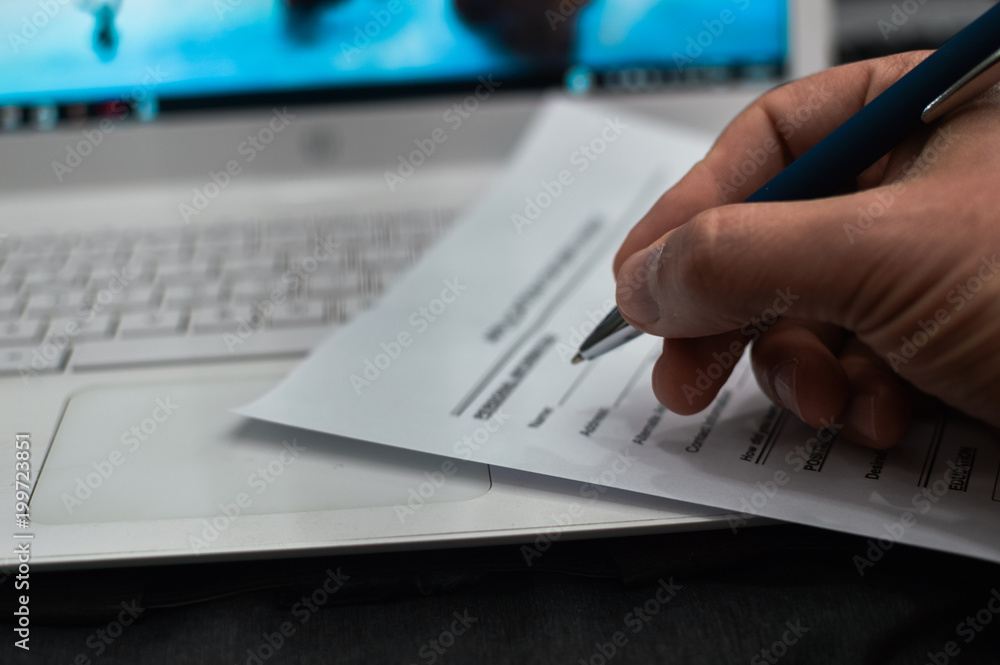 Closeup on hand of a person signing document contract form on light table background Closeup on hand of a person signing document contract form on light table background