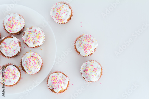 Muffins, cakes with confectionery on a white plate, top view