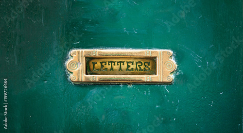 Old mail letter box on a green painted front door, text letters