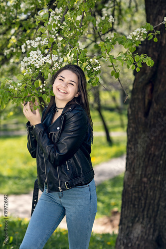 Glamorous young caucasian woman in black leather jacket in a flowery garden