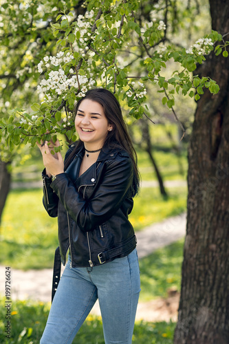 Glamorous young caucasian woman in black leather jacket in a flowery garden