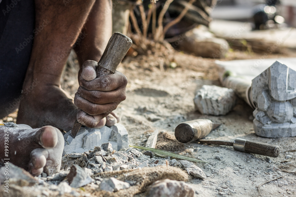 Man barefoot sculpting a rock with a chisel at Chamundi Hills in Mysore ...