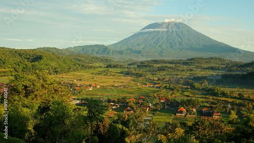 malerischer Vulkan Mt.Agung hinter grünen Reisfeldern und vereinzelten Häusern