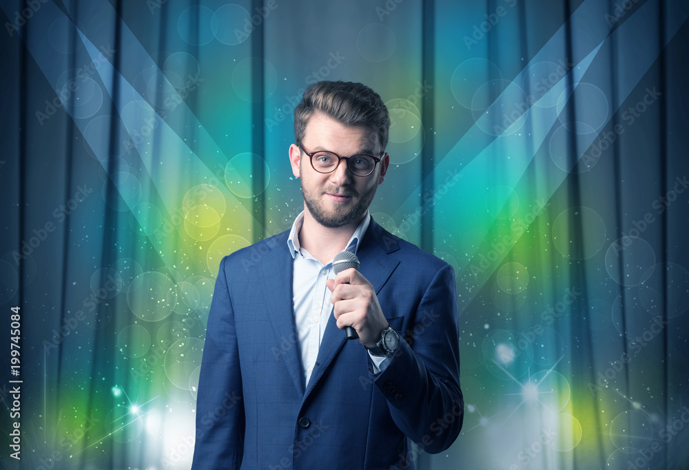 Businessman speaking into microphone with blue curtain behind him Businessman speaking into microphone with blue curtain behind him