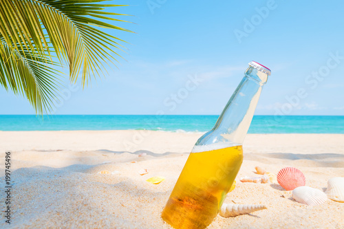 Beer bottle on a sandy beach with palm tree. vintage color tone effect © jakkapan