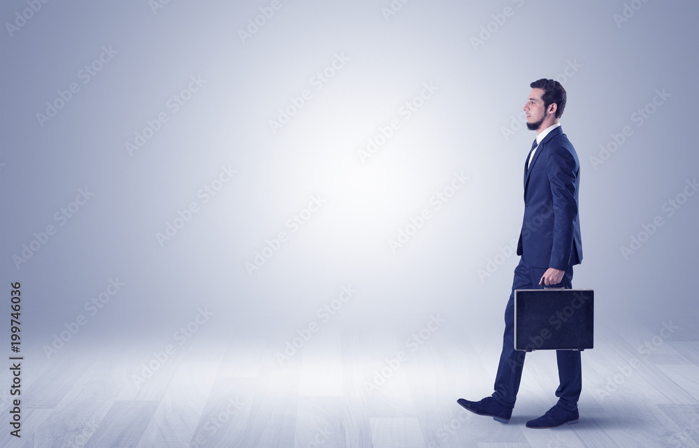 Fototapeta premium Successful businessman walking in front of an empty wall with briefcase on his hand 