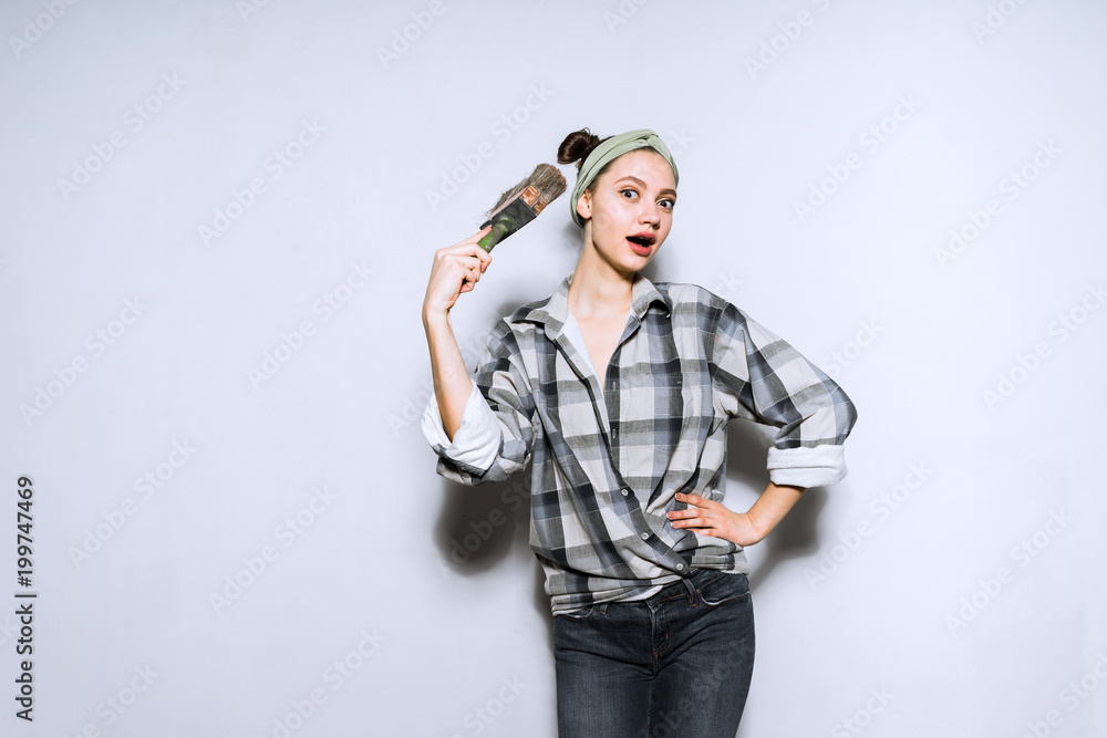 funny surprised girl in a plaid shirt doing repairs in the apartment, holding a brush for painting the walls funny surprised girl in a plaid shirt doing repairs in the apartment, holding a brush for painting the walls