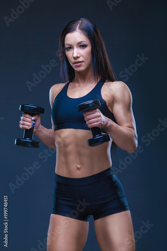 Brutal athletic sexy woman pumping up muscules with dumbbells. The concept of exercise sports, advertising a gym.