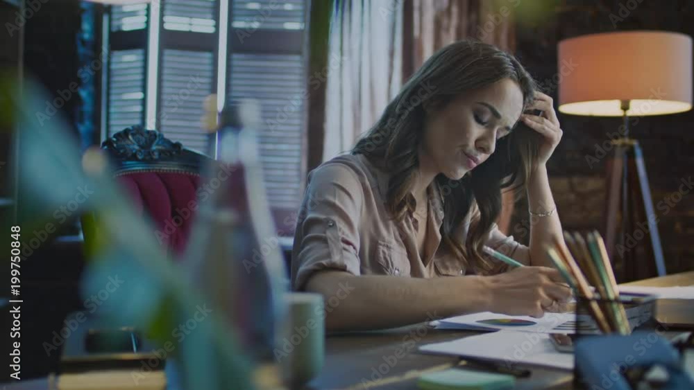 Concentrated businesswoman making notes at table with laptop in office. Focused woman analyzing data graphics. Woman professional thinking on market graph at evening. Business manager work late