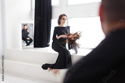 Groom's reflection in mirror. Bride sitting on stairs in white studio photo