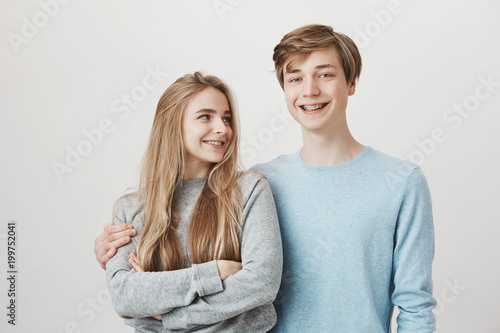 Girlfriend knows boyfriend prepared something for anniversary. Portrait of two friendly caring siblings, hugging and smiling broadly, wearing shiny braces. Girl looking at guy who dare to cuddle her