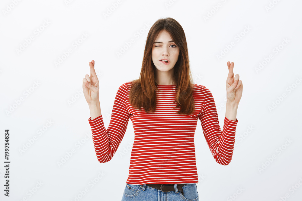Peeking to see good opportunity for action. Indoor shot of creative good-looking female student raising hands with crossed fingers, biting lip and looking with one eye at camera, hoping or praying Peeking to see good opportunity for action. Indoor shot of creative good-looking female student raising hands with crossed fingers, biting lip and looking with one eye at camera, hoping or praying