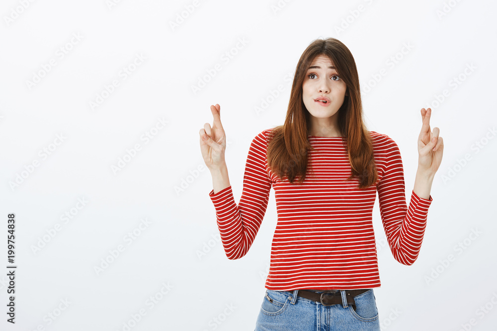 Girl hopes delivery guy will come in time. Portrait of worried impatient young woman in striped outfit, crossing fingers and biting lip, looking aside at clock, wishing or praying for something happen Girl hopes delivery guy will come in time. Portrait of worried impatient young woman in striped outfit, crossing fingers and biting lip, looking aside at clock, wishing or praying for something happen