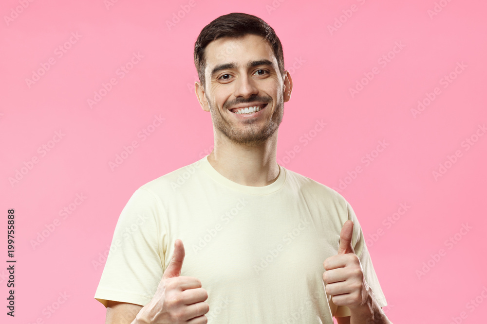 Young optimistic man isolated on pink background showing thumbs up with positive emotions of content and happiness. Concept of satisfaction with quality and recommendation Young optimistic man isolated on pink background showing thumbs up with positive emotions of content and happiness. Concept of satisfaction with quality and recommendation