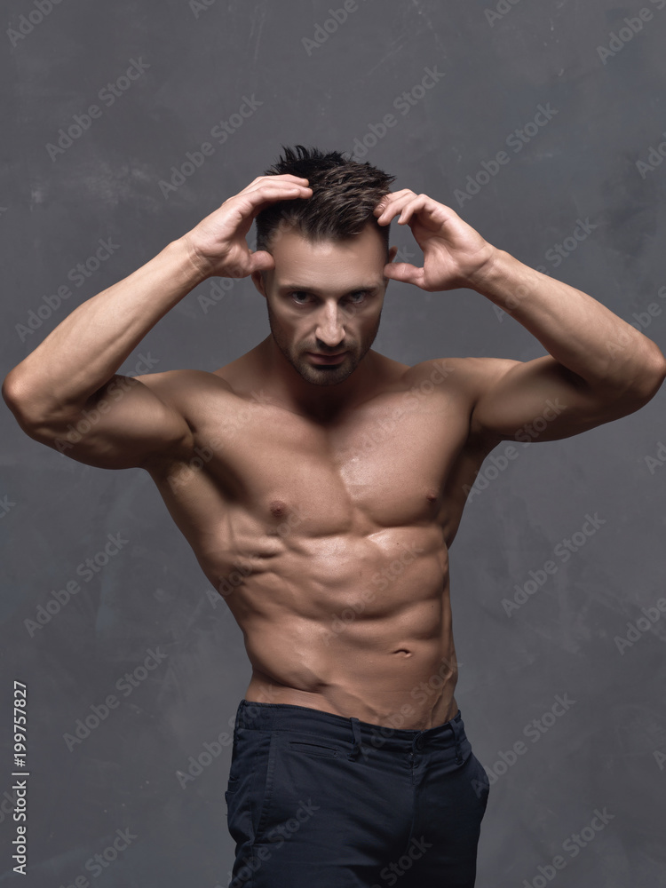 A young man with trained muscles posing near the wall.
