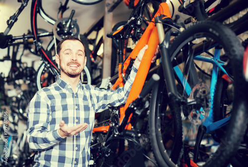 positive man in bicycle shop chooses for himself sports bike