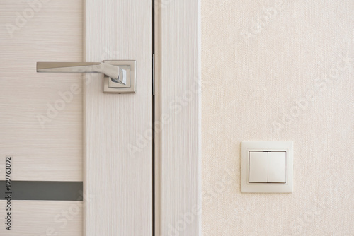 Beige light switch installed next to the door on the wall © pridannikov