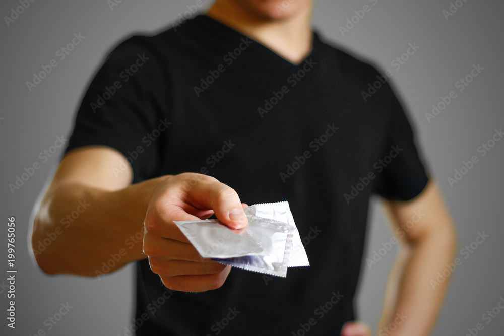 Man's hand holding a single condom. Close up. Isolated on grey background Man's hand holding a single condom. Close up. Isolated on grey background