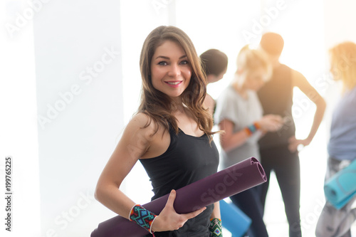 Portrait of young beautiful yoga woman holding exercise mat while practicing yoga at the gym studio