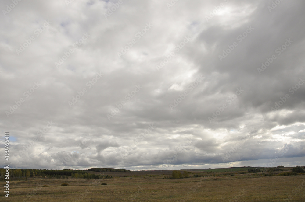 Heavy grey clouds in the cold autumn sky over fields, forests and mountains Heavy grey clouds in the cold autumn sky over fields, forests and mountains