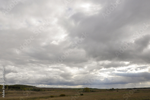 Heavy grey clouds in the cold autumn sky over fields, forests and mountains