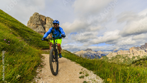 Tourist cycling in Cortina d'Ampezzo, stunning Cinque Torri and Tofana in background. Man riding MTB enduro flow trail. South Tyrol province of Italy, Dolomites.