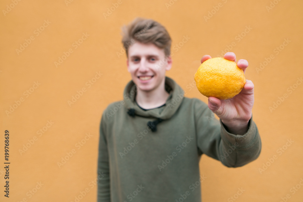 Happy man standing on an orange background with lemon in his hands. Focus on lemon. Happy man standing on an orange background with lemon in his hands. Focus on lemon.