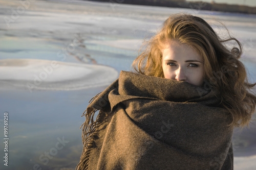 Woman wrapped in gray big blanket in snowy winter park. Winter concept. photo