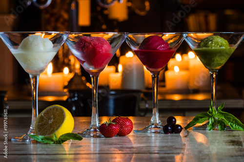 Four kinds of natural colourful sorbet decorated by lemon, mint, strawberry, blueberry and basil in front of candles on the bar counter. Natural ice cream photo