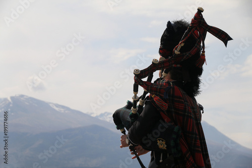 mężczyzna w tradycyjnym szkockim stroju grający na kobzie oraz najwyższy szczyt szkocji w tle