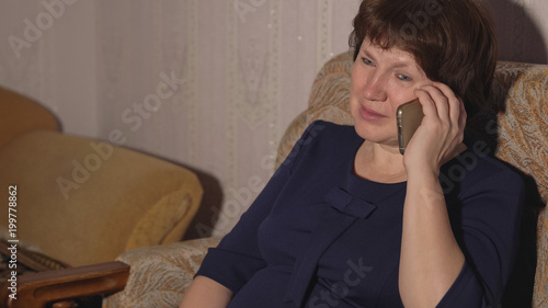 Woman in a blue dress is sitting in a chair and talking on the phone