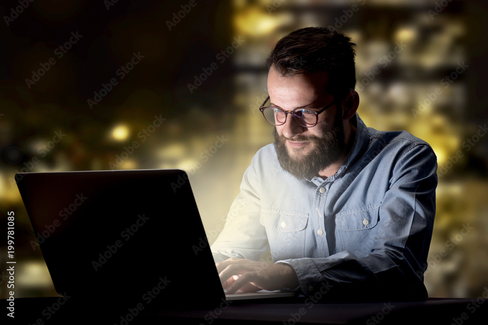 Young handsome businessman working late at night in the office with city lights in the background Young handsome businessman working late at night in the office with city lights in the background