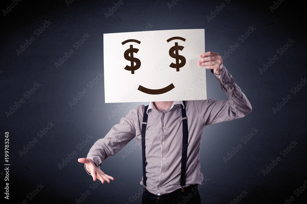 Young casual businessman hiding behind a greedy face drawing on cardboard Young casual businessman hiding behind a greedy face drawing on cardboard