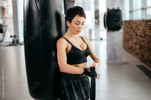 side view shot of young pretty athlete with dark hair in black shorts and top putting on boxing bandage indoor. active life. be fong of sport photo