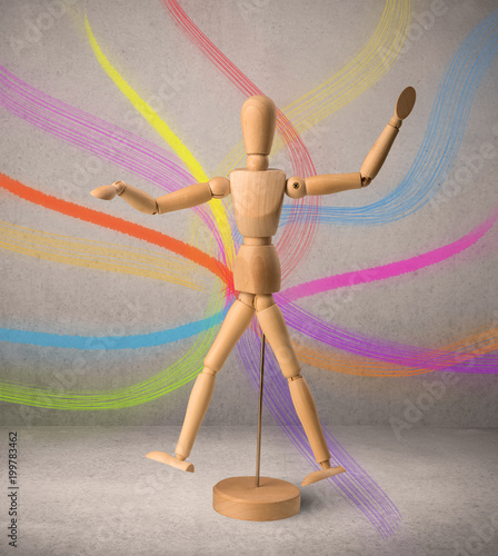 Wooden mannequin posed in front of a greyish background with colorful lines behind it