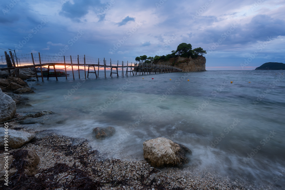 Beautiful sunrise, just before the storm rains. The famous Cameo island. A beautiful small island with wooden bridge and turquoise water. Zakynthos, Greece.