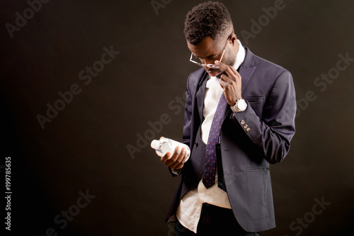 close up portrait of black guy in fashionable suit with mineral water after crapulence hangover isolated on the black background. satisfy thirsty. look at the bottle photo